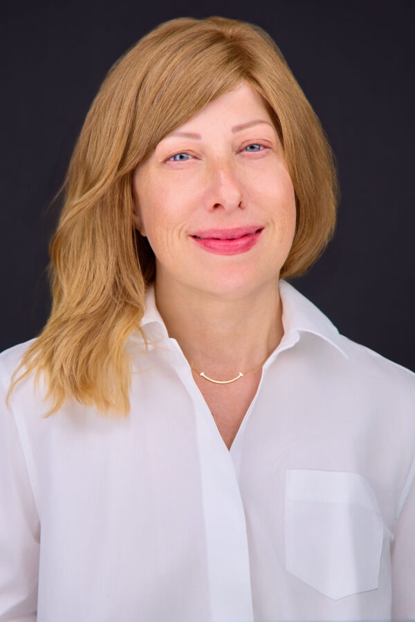 Professional headshot of a person with shoulder-length auburn hair wearing a white collared shirt against a dark background.