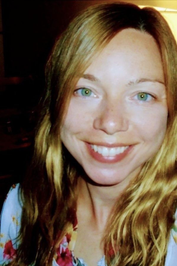 Person with reddish-brown hair and green eyes smiling at camera, wearing a colorful floral top.