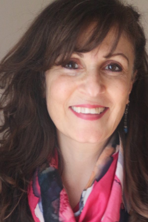 Professional headshot of a smiling person with long dark hair with bangs, wearing pink lipstick and a colorful scarf.