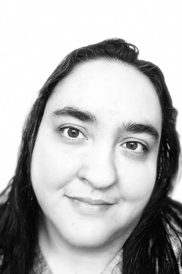 Black and white portrait of a person with long dark hair and defined eyebrows, looking directly at camera against a white background.