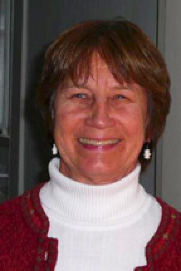 Person with shoulder-length reddish-brown hair wearing a burgundy cardigan over a white turtleneck, smiling at the camera.