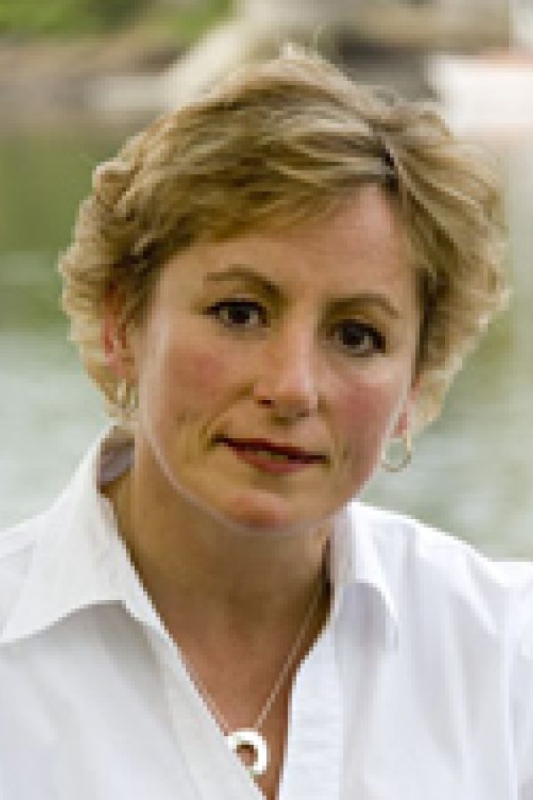 Person with short blonde hair wearing a white collared shirt, smiling at the camera outdoors.