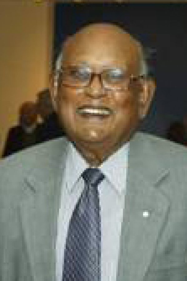 Person wearing glasses and gray suit with blue tie, smiling at camera indoors.