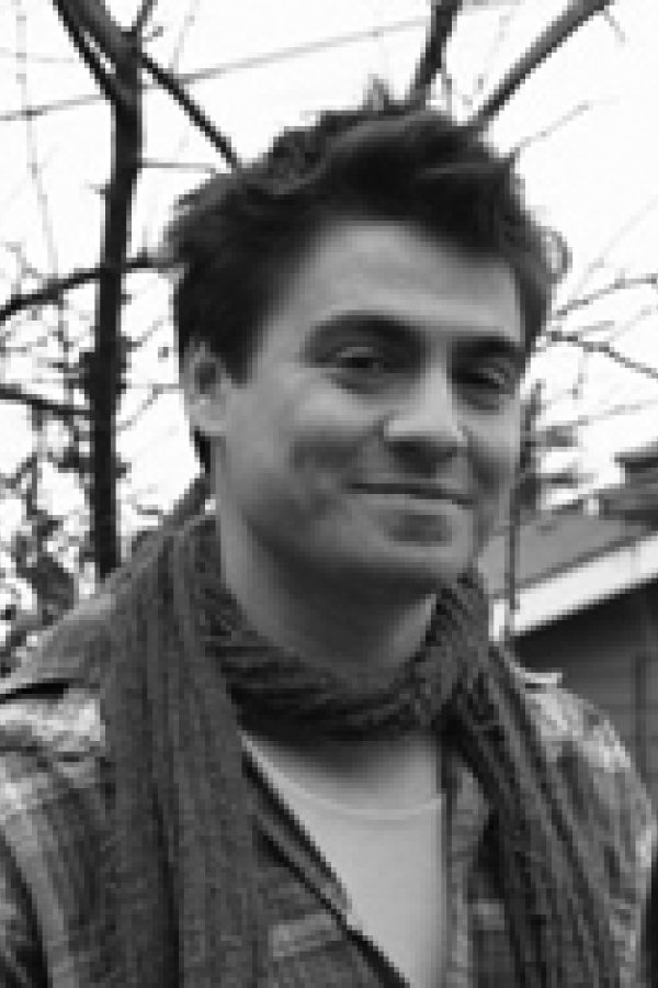 Black and white portrait of a person with dark hair against a blurred background of bare tree branches.