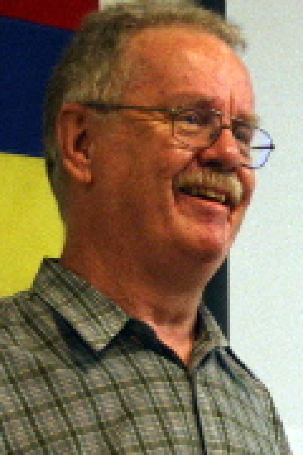 Person wearing glasses and a plaid shirt, smiling, standing in front of a colorful abstract background.