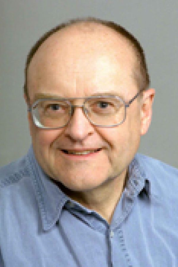 Person wearing glasses and light blue shirt smiling at camera against gray background.