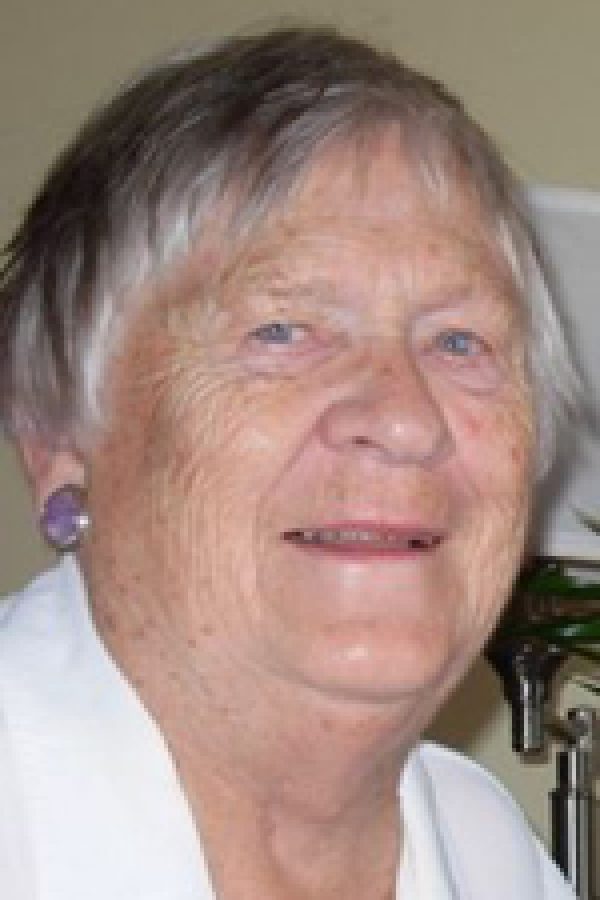 Older person with gray hair wearing a white shirt, smiling at the camera indoors.