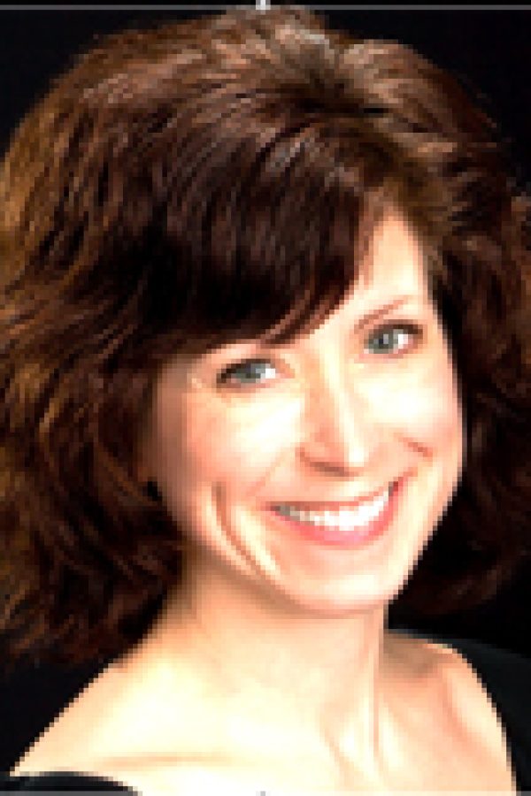 Portrait of a smiling person with shoulder-length brown wavy hair against a dark background.
