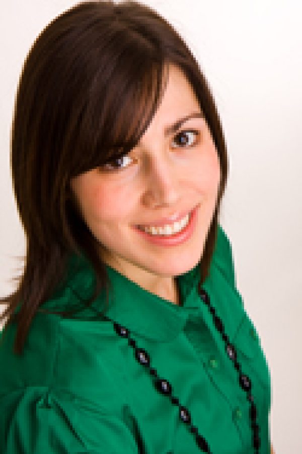 Person with dark hair and bangs wearing a green shirt against a white background, smiling at the camera.
