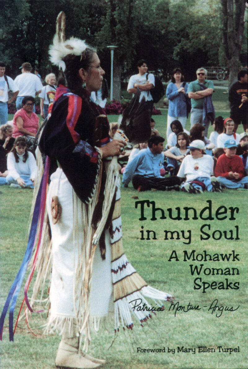 Person in traditional Mohawk regalia speaking to seated gathering in park, book cover for "Thunder in my Soul" by Patricia Monture-Angus.