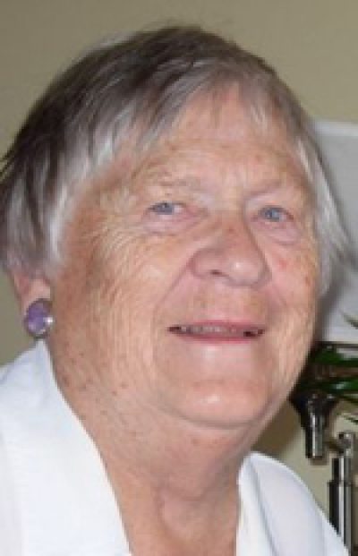 Older person with gray hair wearing a white shirt, smiling at the camera indoors.