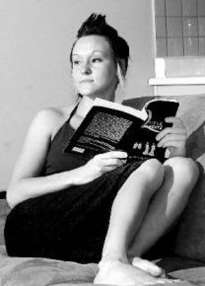 Person in black sleeveless dress sitting and holding an open book, looking upward in black and white photograph.