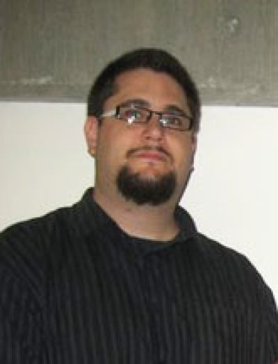 Person wearing glasses and a dark pinstriped sweater against a neutral background.