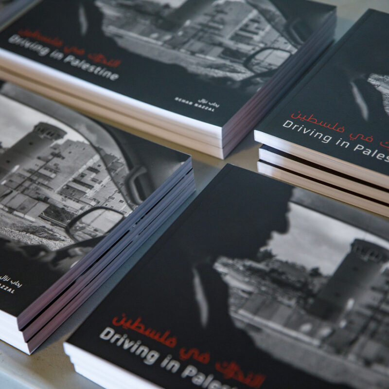 Several copies of "Driving in Palestine" books with black and white photographs stacked on a surface.