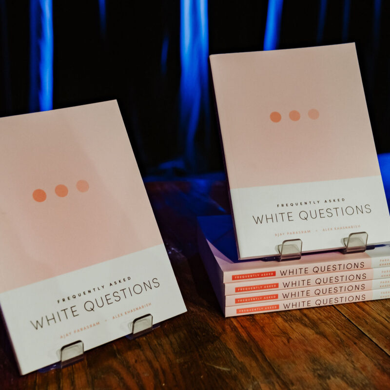 Copies of "White Questions" by Frequently Asked displayed on a wooden surface with blue lighting in the background.