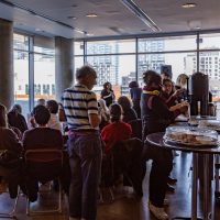 Group of people gathered in a high-rise meeting space with floor-to-ceiling windows overlooking a city skyline.