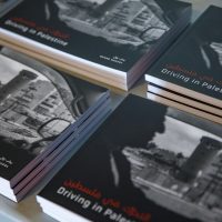 Several copies of "Driving in Palestine" books with black and white photographs stacked on a surface.