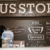 Bus Stop storefront with chalkboard menu displaying wine options and specials, including Vivo White and Red wines.